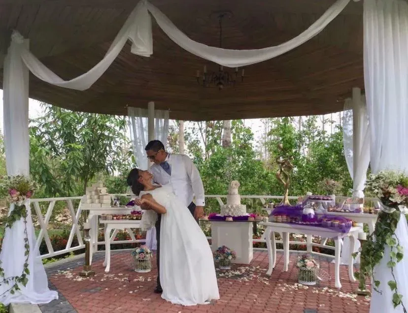 Novio inclinando a la novia en la glorieta decorada con telas blancas de Casa Grande Resort