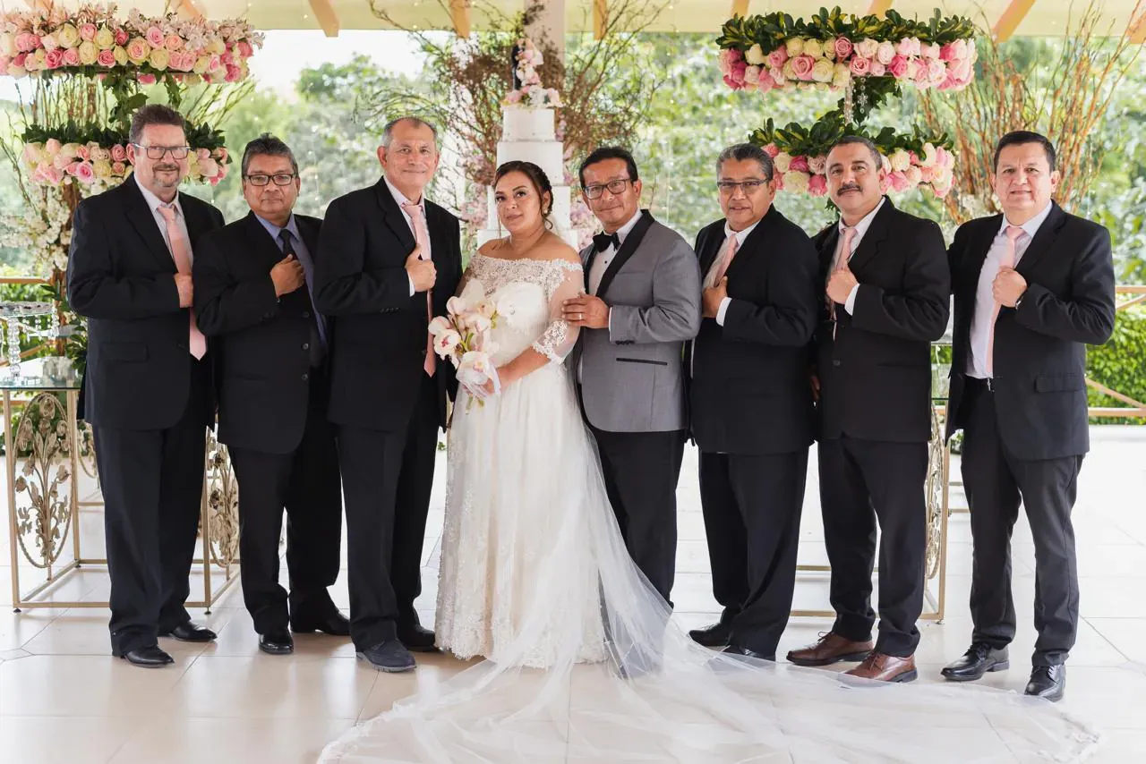 Novios junto a seis padrinos de traje oscuro frente al pastel de bodas en Casa Grande Resort
