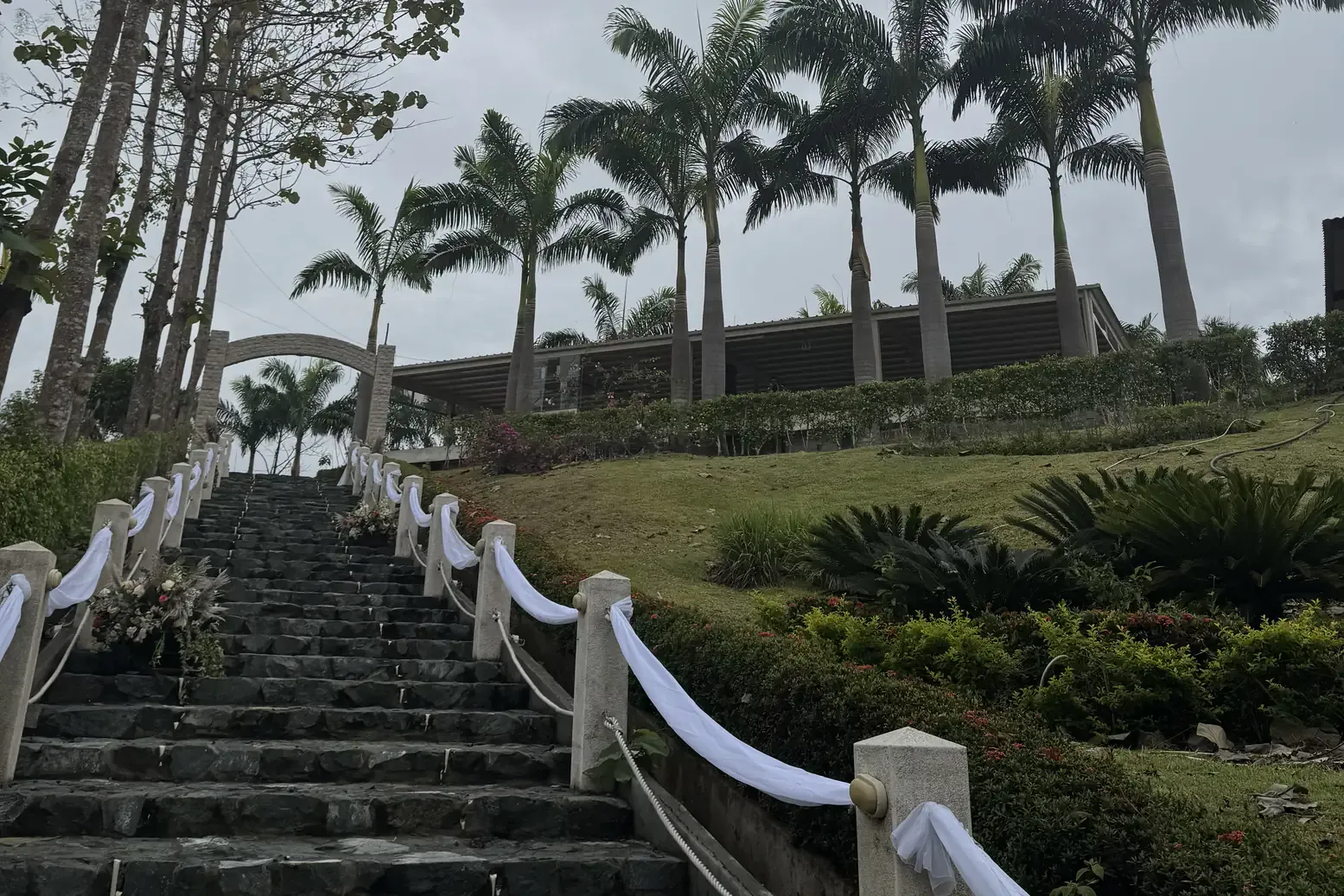 Escalinata de piedra adornada con telas blancas junto a un jardín con palmeras en Casa Grande Resort