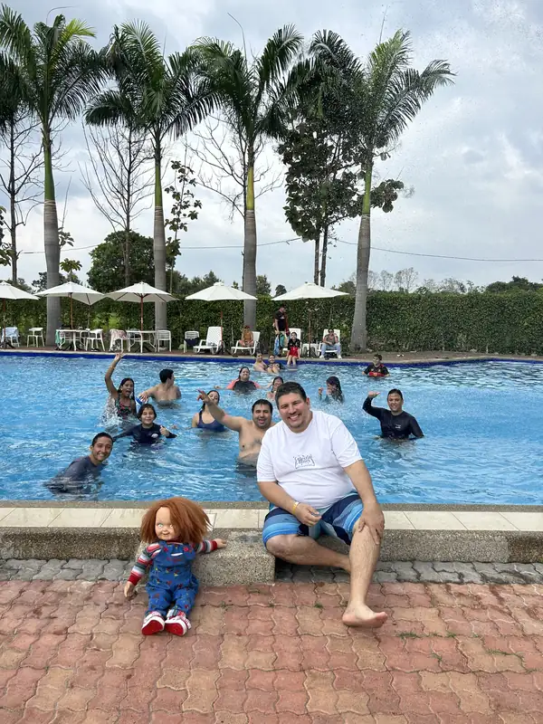 Visitante sentado al borde de la piscina mientras un grupo saluda desde el agua en Casa Grande Resort