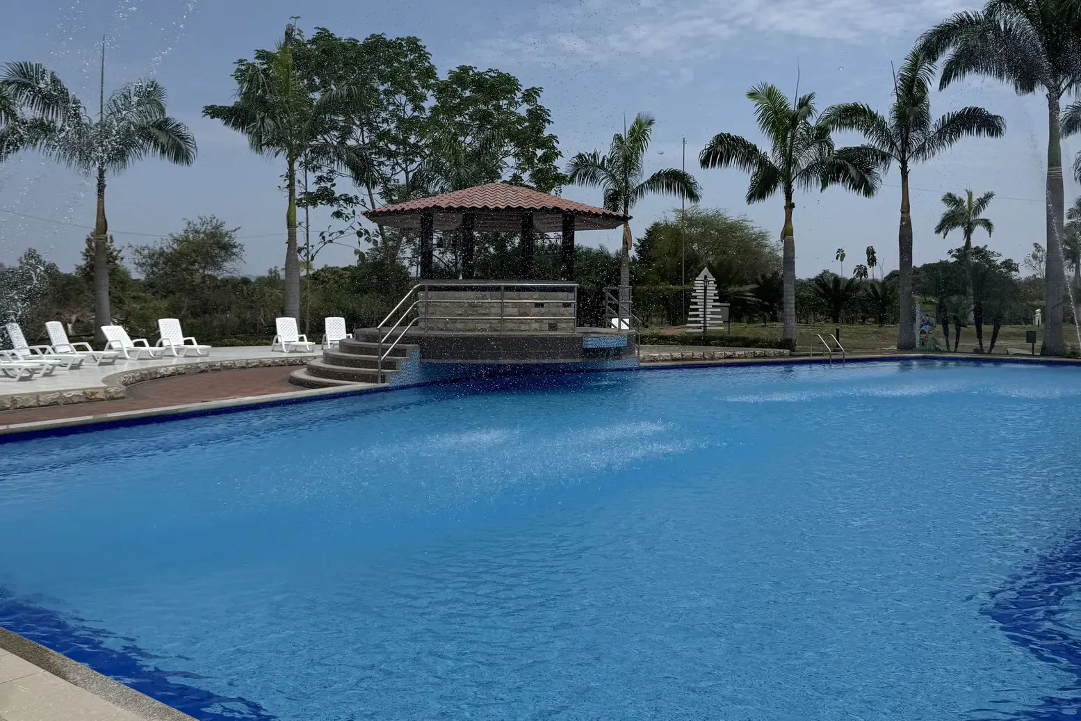 Piscina con chorros de agua y kiosko entre palmeras en Casa Grande Resort