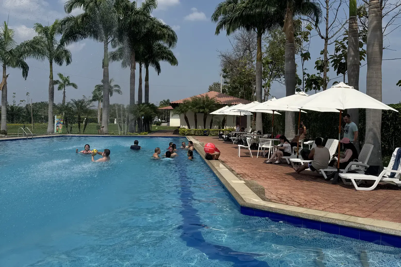 Visitantes nadando en la piscina con sombrillas y palmeras de Casa Grande Resort